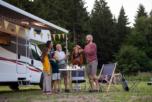 Große Familie steht an einem Campingtisch vor ihrem Wohnwagen