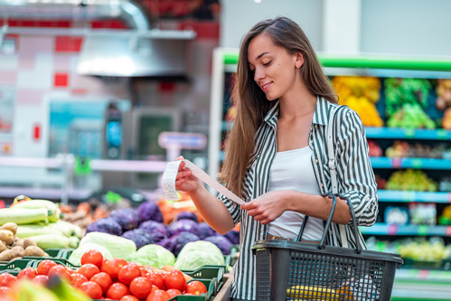 Frau mit Einkaufskorb sieht sich ihren Kassenbeleg im Supermarkt an