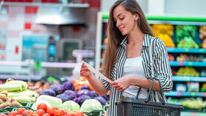 Frau mit Einkaufskorb sieht sich ihren Kassenbeleg im Supermarkt an